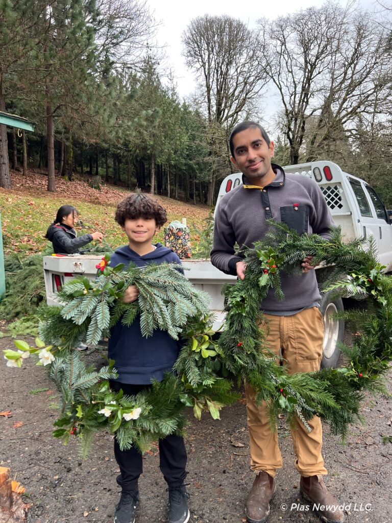 A young man and a gentleman standing in front of a white truck holding wreaths they just made.